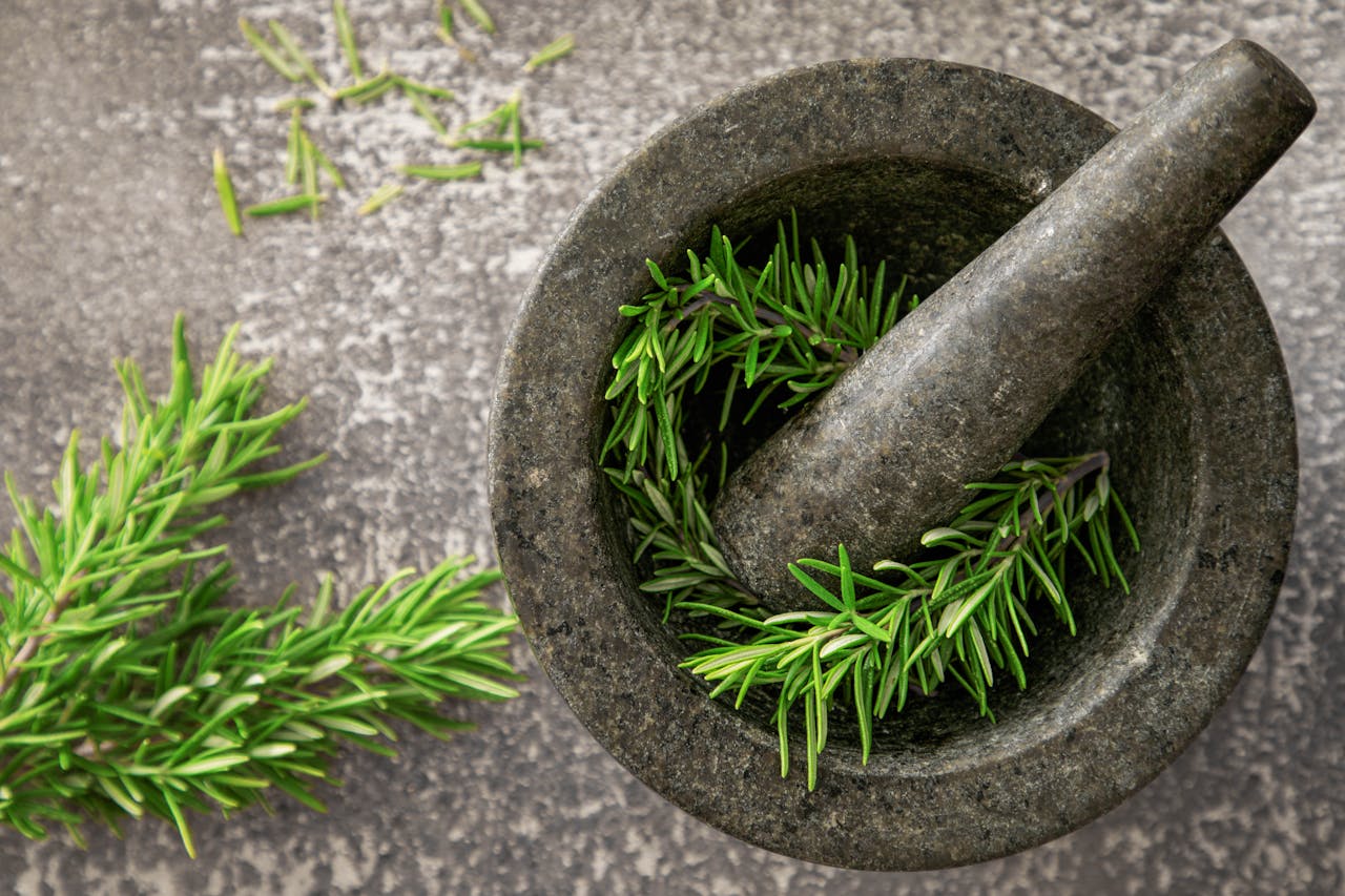 Close-up of fresh rosemary sprigs in a stone mortar and pestle, highlighting natural herbs.