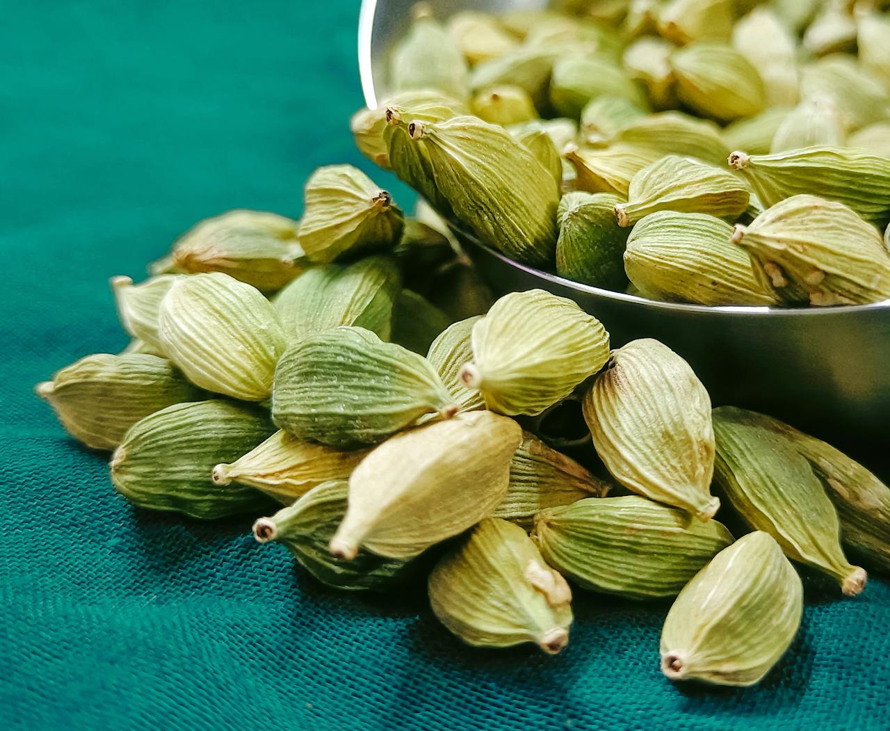 A detailed close-up of fresh organic green cardamom pods on a textured surface.